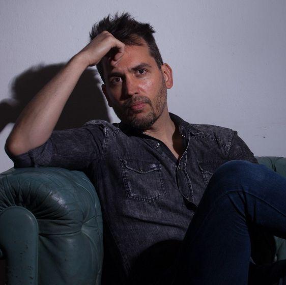 Plano medio de Maximiliano Poter, tallerista de Ciempiés. Maximiliano, delgado y de cabellos cortos castaños, está sentado en un sillón verde.