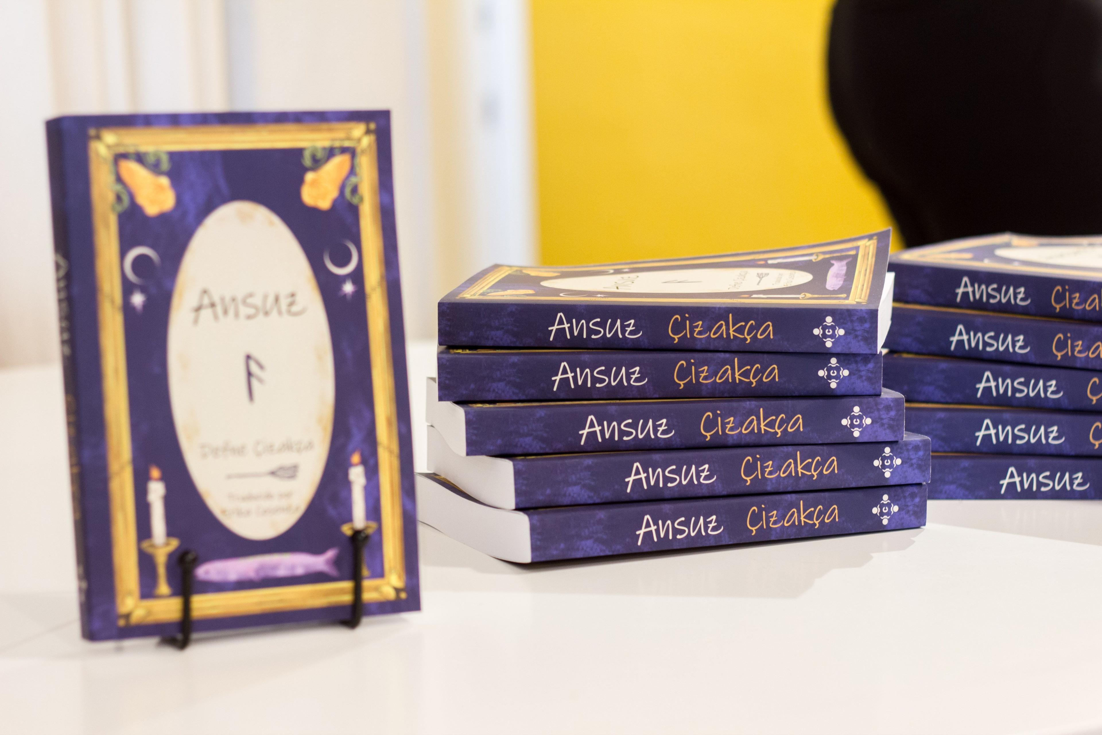 Foto tomada por Gigi Caffarena durante la presentación del libro Ansuz en Barcelona. Sobre una mesa hay un atril aque sostiene un ejemplar de manera tal que se vea la portada; a su lado, una pila con cinco ejemplares que muestran el lomo hacia la cámara.