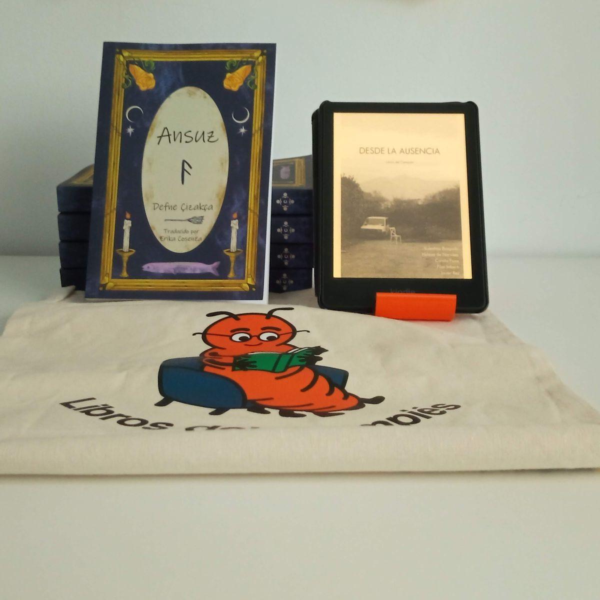 Fotografía de un ejemplar de "Ansuz" y de un Kindle que muestra "Desde la ausencia". Ambos están apoyados sobre una bolsa en color crema que tiene la mascota de Libros del Cimpiés.