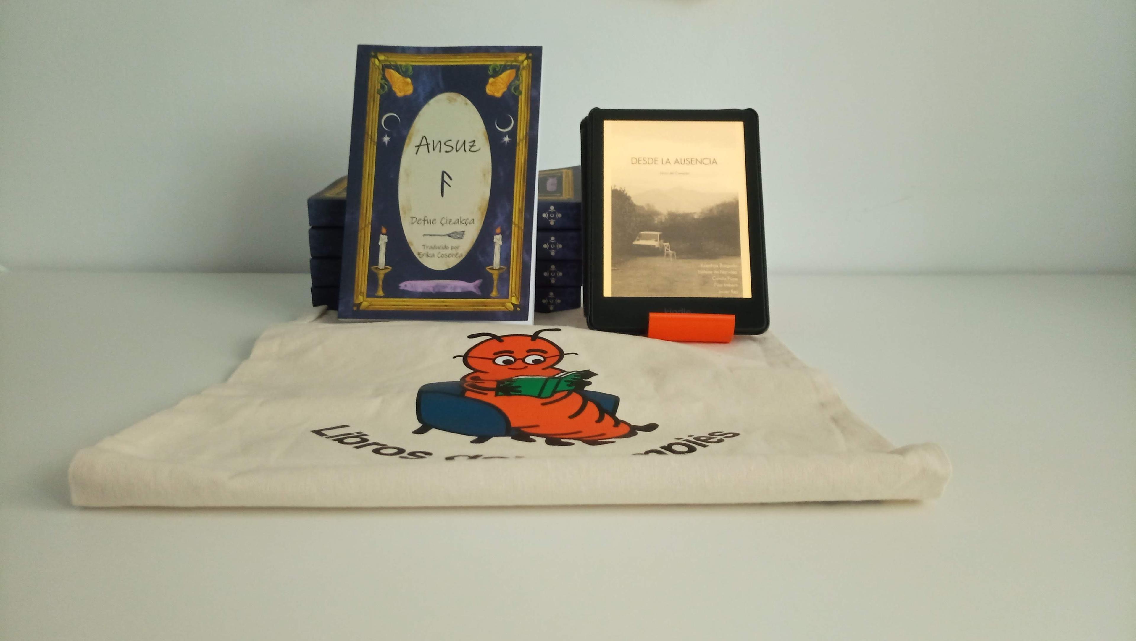 Fotografía de un ejemplar de "Ansuz" y de un Kindle que muestra "Desde la ausencia". Ambos están apoyados sobre una bolsa en color crema que tiene la mascota de Libros del Cimpiés.